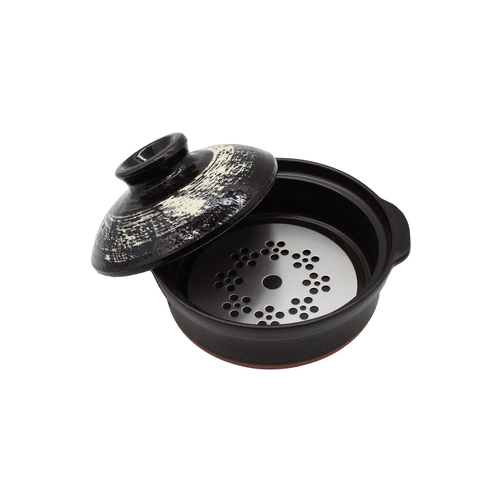 The Black Earthenware Donabe Pot with White Brushstroke Design features a partially open black ceramic lid, a metal steamer insert with circular holes inside, and is induction compatible for versatile cooking.