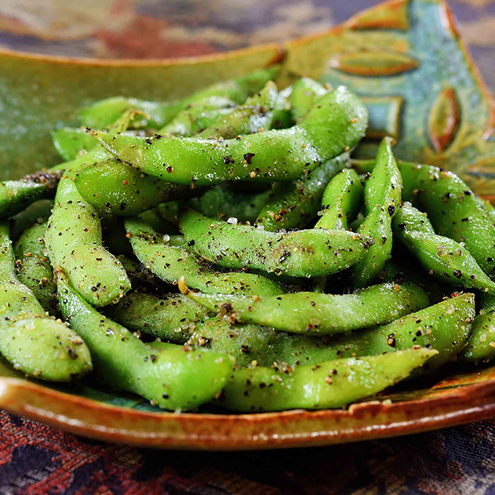 Enjoy a delicious and nutritious snack with edamame pods, harvested from Edamame Bean Plants x 3, lightly seasoned with salt and black pepper on a decorative green and brown dish.
