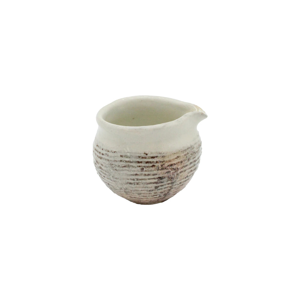 
                  
                    The Pourer - Fuchiara Carved is a small, round Japanese ceramic pourer with a textured base and spout in off-white and light brown, inspired by Shigaraki pottery, shown on a plain white background.
                  
                