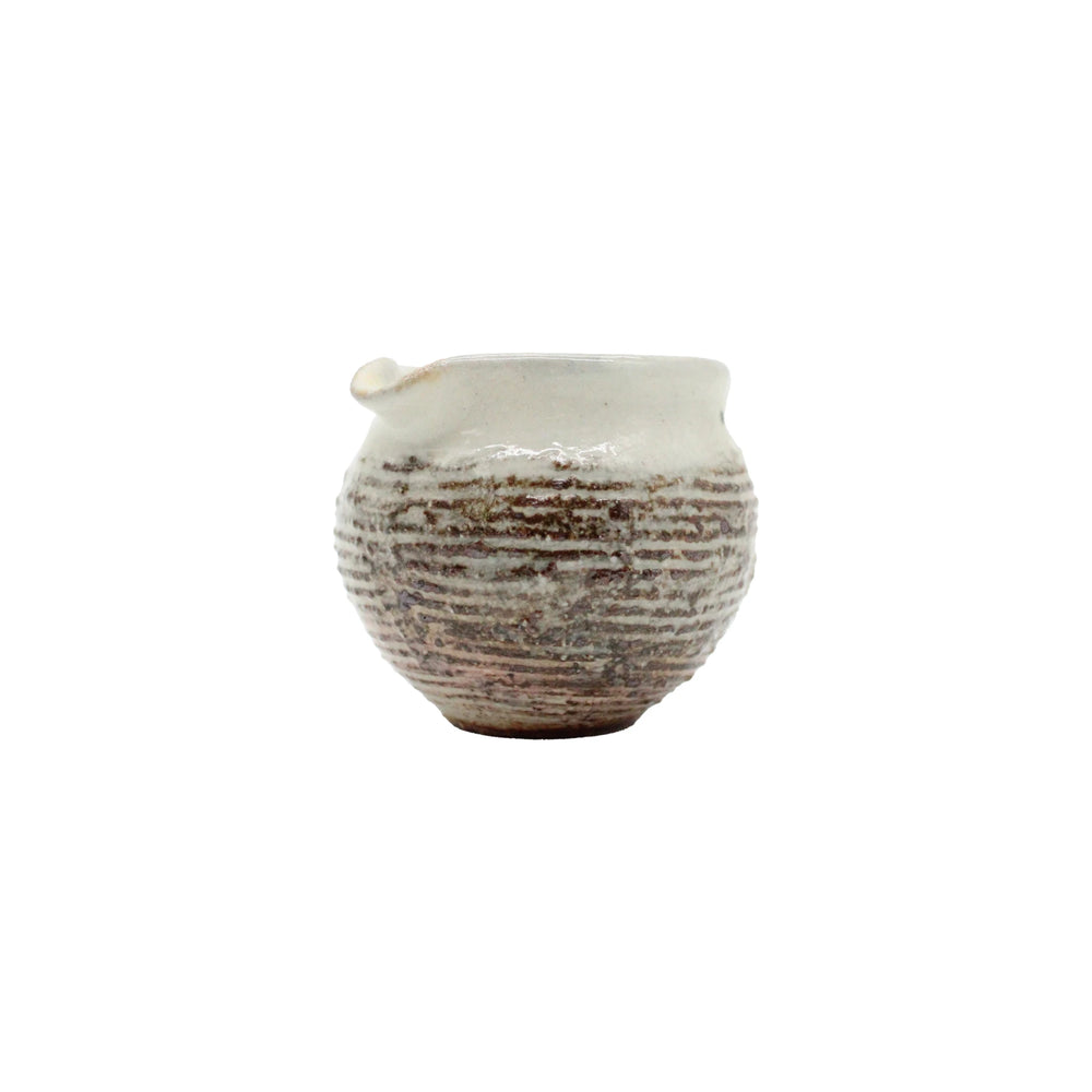
                  
                    The Pourer - Fuchiara Carved is a small, round Japanese pourer made from textured ceramic with a narrow opening and spout. It features a white, slightly uneven glaze with horizontal ridges inspired by Shigaraki pottery artistry.
                  
                