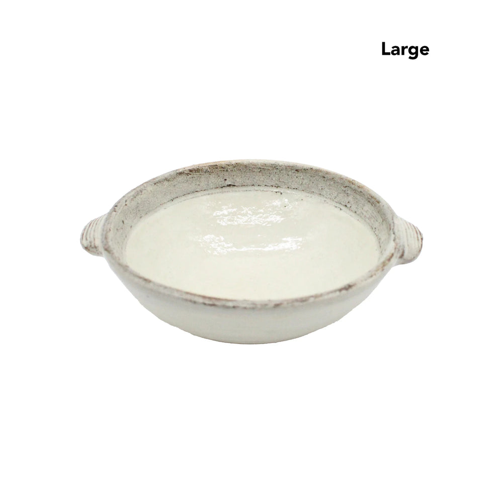 
                  
                    A large, round, shallow ceramic dish called the Ear Bowls - Fuchiara Carved, with two small handles and a refined Kohiki finish, contains a white liquid.
                  
                