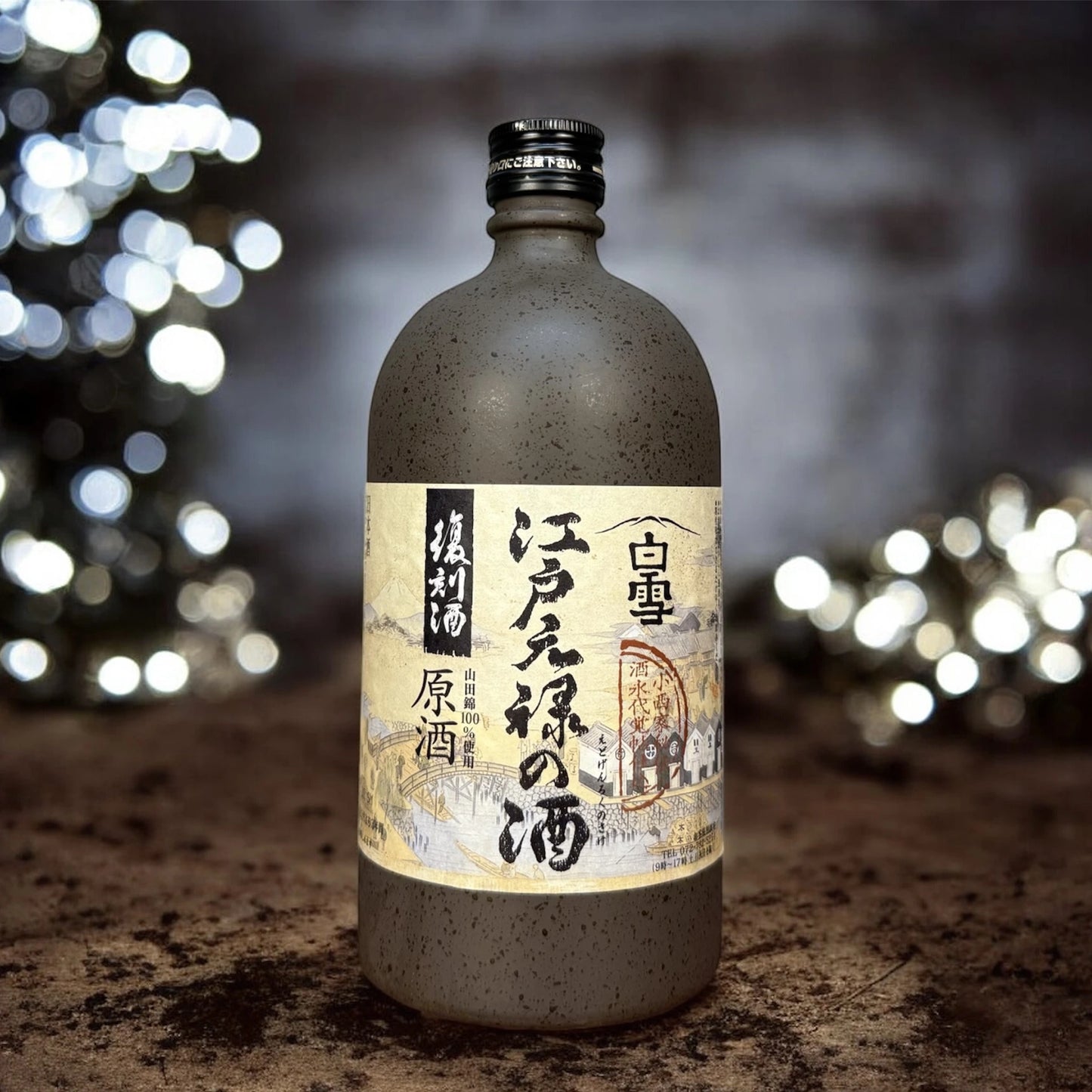 
                  
                    A 720ml bottle of Genroku Redux Sake from Konishi Shuzo, with a beige label and black kanji, is displayed on a textured surface against a backdrop of blurred lights.
                  
                