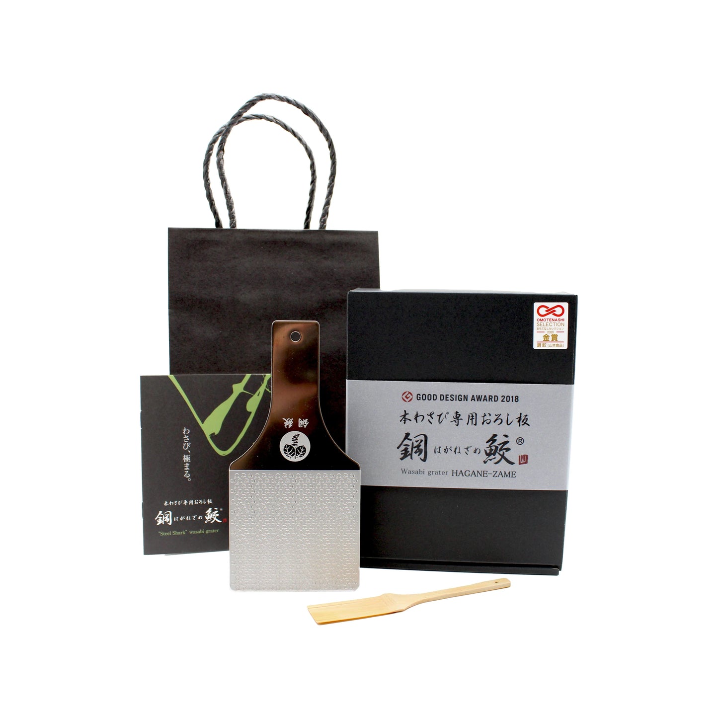 The Hagane-zame Wasabi Graters set includes a metal wasabi grater, wooden spatula, black gift bag, booklet, and a black box with Japanese text and the Good Design Award label.