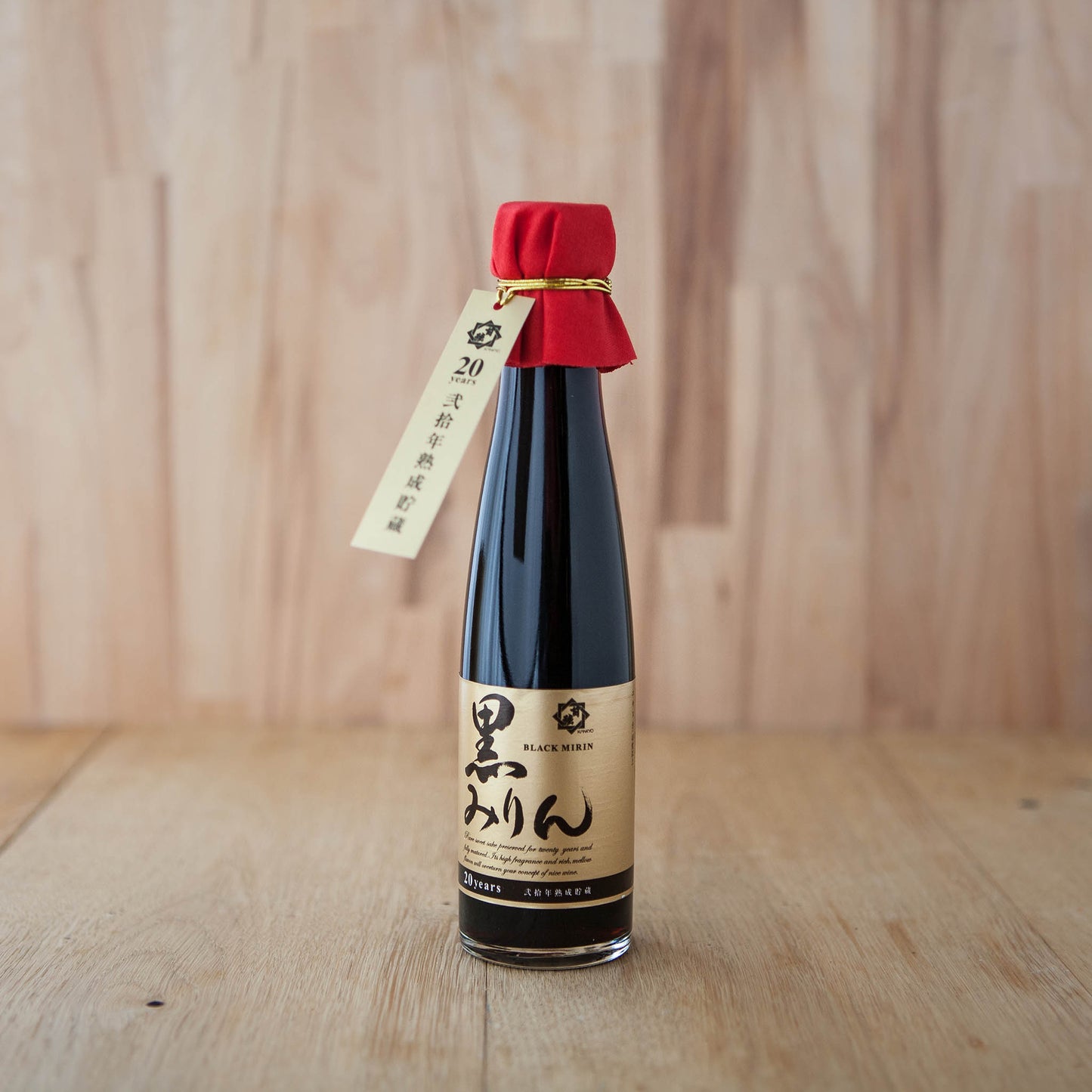 
                  
                    A tall glass bottle of 20 Year Aged Black Hon Mirin with a gold label and red cloth on the cap, set against a light wooden background—highlighting its natural and pure essence.
                  
                