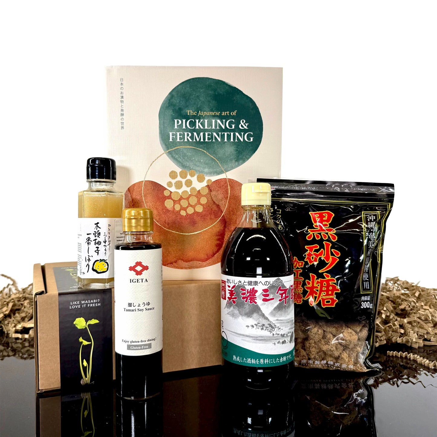 The Japanese Art of Pickling & Fermenting Set features Japanese foods and a pickling book, beautifully arranged on black with shredded brown paper, perfect for celebrating traditional Japanese pickling.