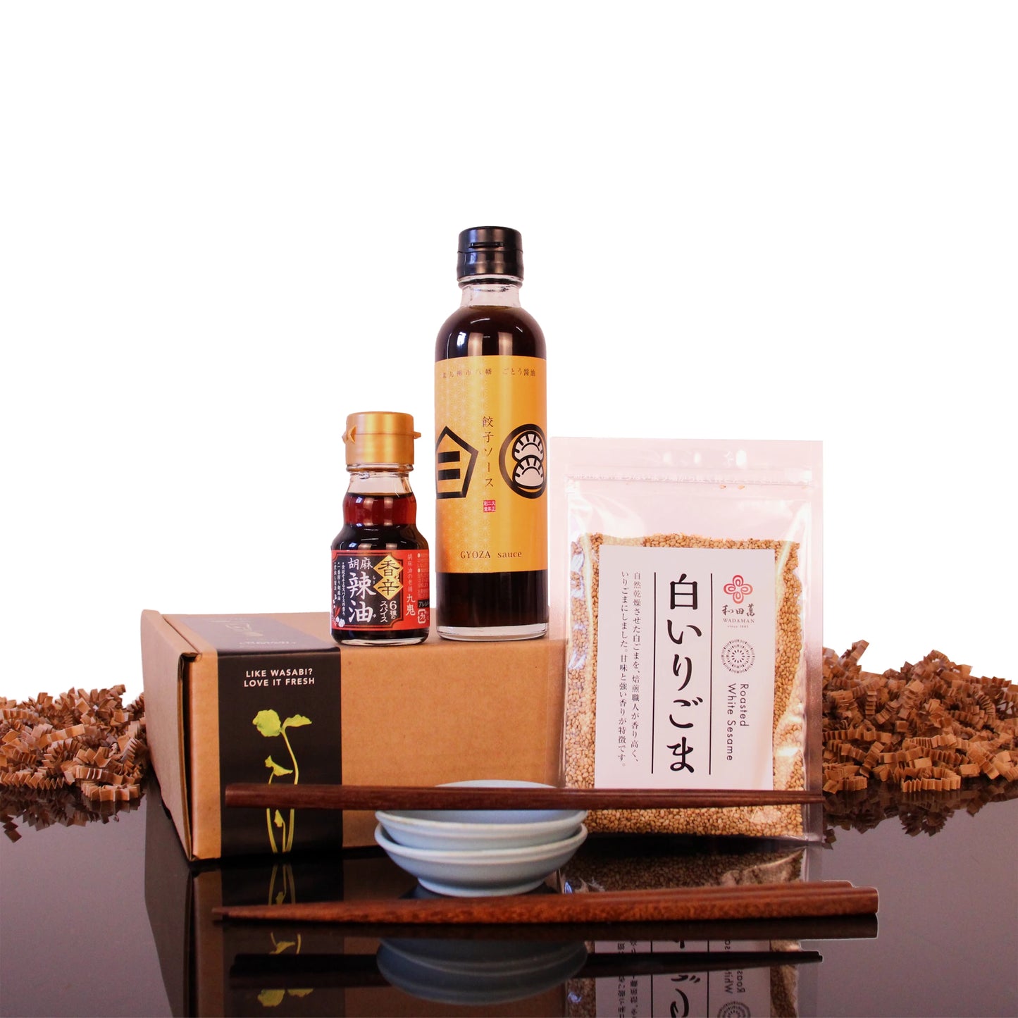 Small bottle of chili oil, bottle of gyoza sauce, bag of white sesame seeds, two dipping bowls, and a pair of chopsticks in front of a Japanese Gyoza Night Set box.