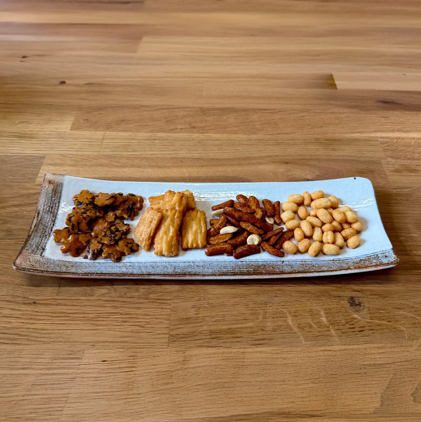 
                  
                    A rectangular plate displays four varieties of Minoya Arare on a wooden table—a delightful Japanese Rice Cracker Set perfect for snack enthusiasts.
                  
                