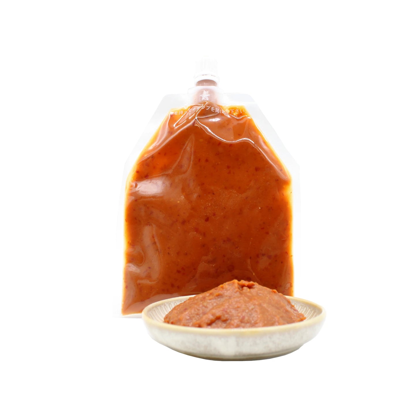 A sealed pouch of Kanzuri Fermented Red Chilli Paste - 100g, made with yuzu citrus, is displayed behind a small dish filled with its vibrant orange-red paste.