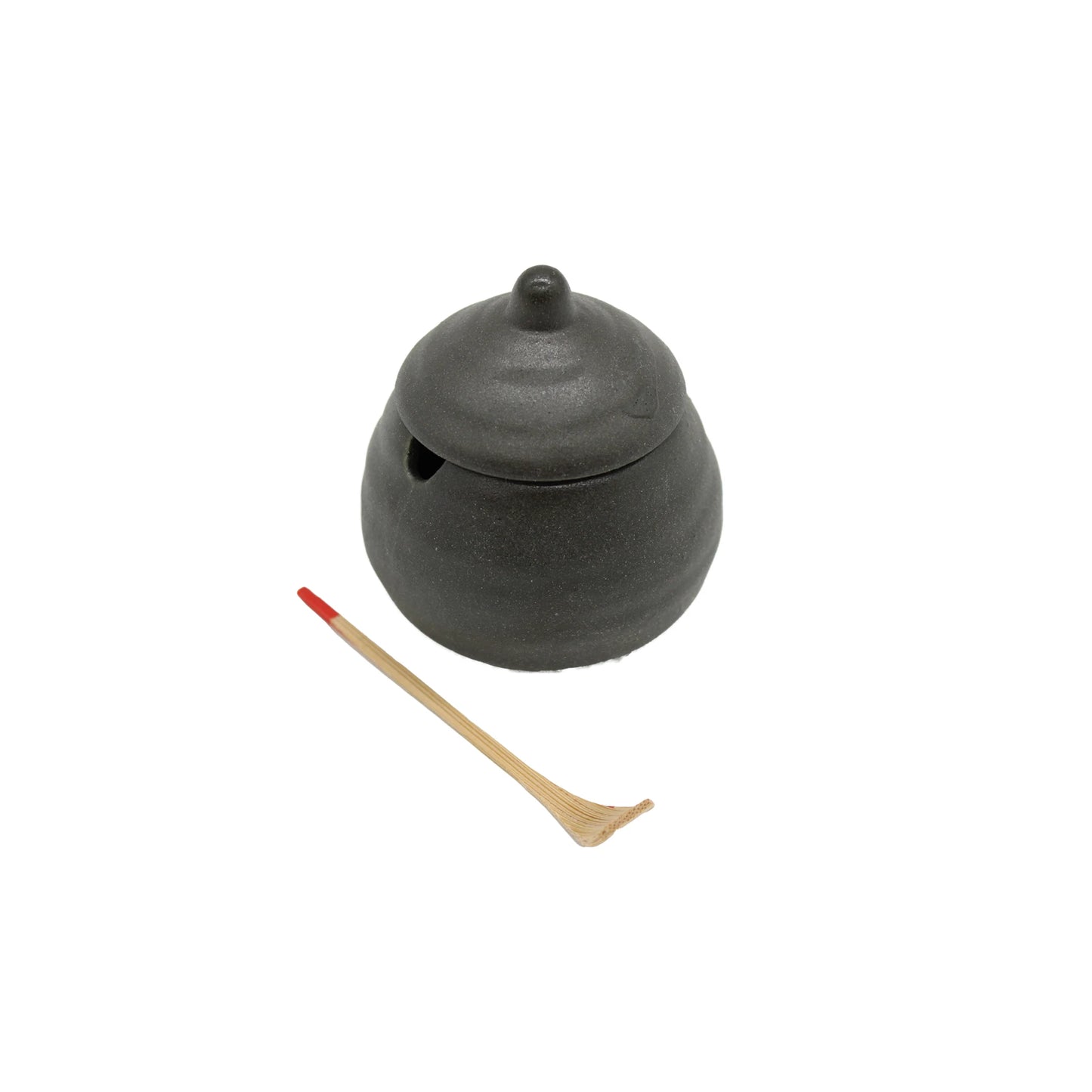 The Karashi / Shichimi Spice Pot - Black Bizen, a black, round pot with a small opening, sits beside a bamboo utensil with a red-tipped handle on a white background.