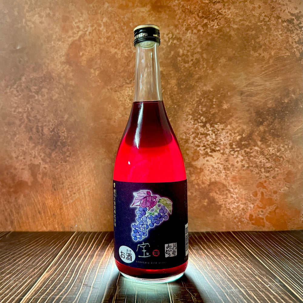 A bottle of Kodakara - Gassan Wild Grape Liqueur 720ml, featuring a dark grape-themed label, rests on a wooden surface with a mottled brown background.
