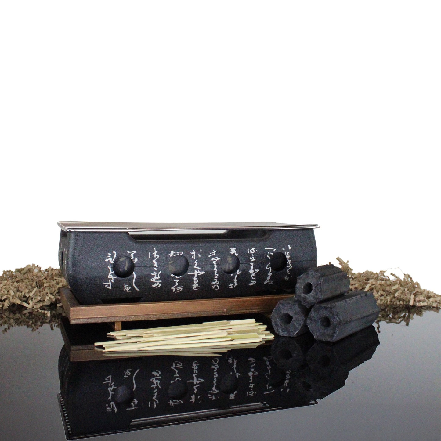 The Konro Aluminium Grill 36cm Barbecue Set, featuring Japanese script and a wooden base, is displayed with Binchotan charcoal briquettes and bamboo skewers on a reflective surface.