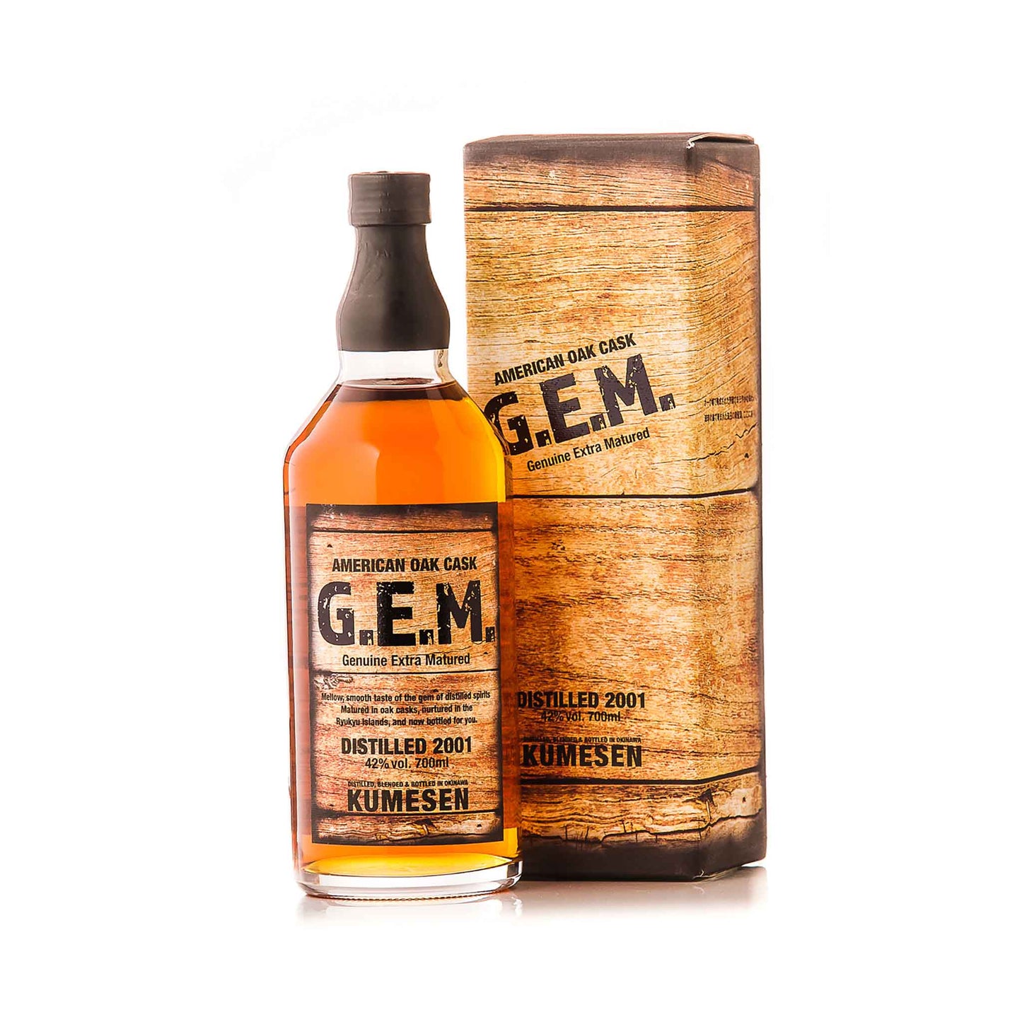 
                  
                    A bottle of Kumesen G.E.M. Awamori 10 Year Aged - 700ml stands beside its wooden-textured cylindrical box, featuring labels stating “Distilled 2001,” “Awamori,” and “Genuine Extra Matured.”.
                  
                
