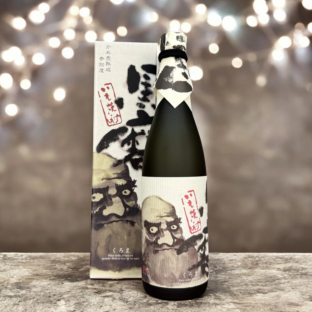 
                  
                    A bottle of Kuroma Sweet Potato Shochu (720ml) with a white label featuring illustrated faces stands before a matching box, set against blurred string lights—reflecting the artistry of Kagoshima’s shochu and black koji heritage.
                  
                