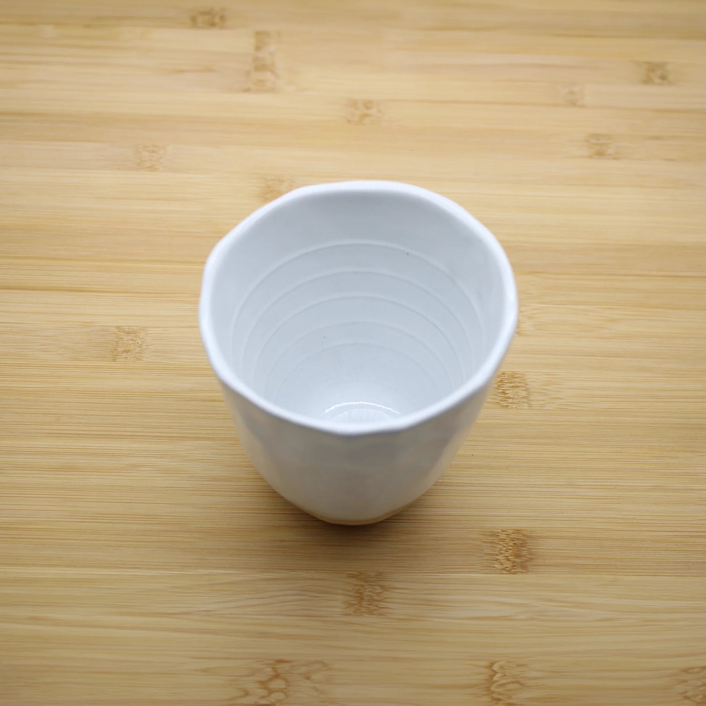 
                  
                    The Lopsided Mug - White And Bisque, featuring a slightly irregular rim and earthenware base, sits on a light wooden surface and reflects Japanese craftsmanship.
                  
                