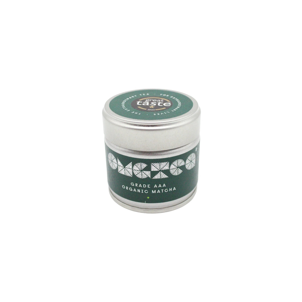 A small silver tin labeled AAA Grade Organic Matcha Green Tea – 30g with a green lid and a decorative white pattern.