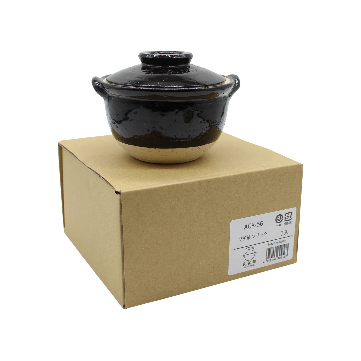 
                  
                    The Mini Donabe Pot - Black, a petite Iga ware ceramic pot with a lid, is displayed atop a plain brown cardboard box featuring a white product label on the side.
                  
                