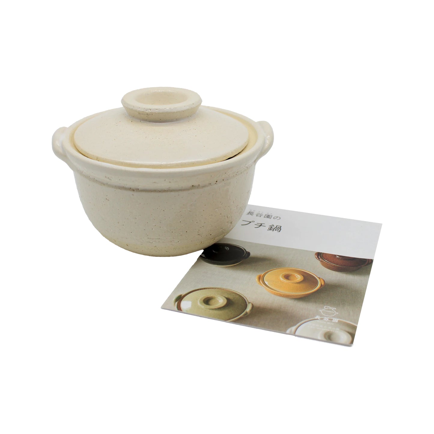 
                  
                    A small, white ceramic Mini Donabe Pot with a lid sits beside a pamphlet displaying images of similar Japanese tableware in various colors.
                  
                