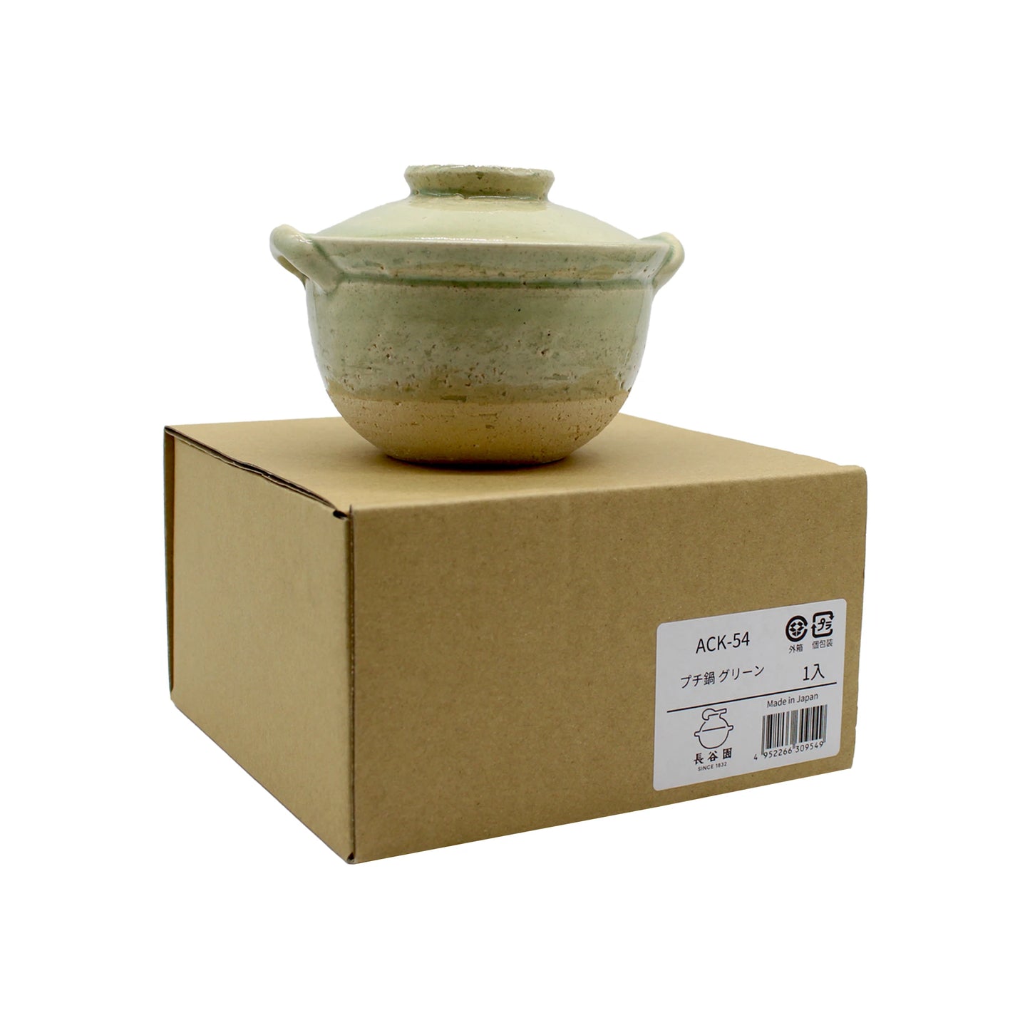 
                  
                    The Mini Donabe Pot - Green, a small ceramic pot with lid and side handles inspired by traditional Japanese tableware, is shown resting atop a closed brown cardboard box with a product label affixed to the side.
                  
                