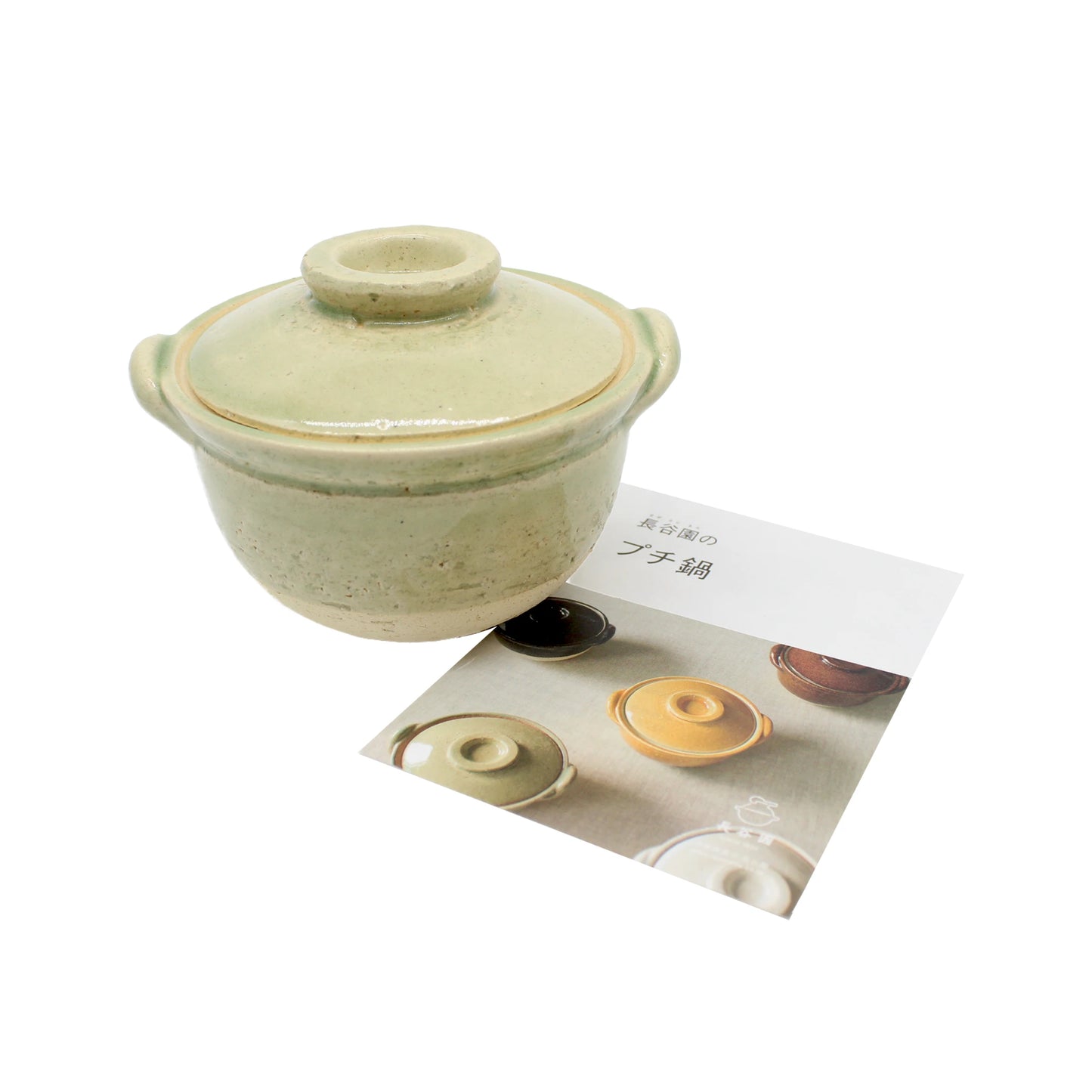 
                  
                    The Mini Donabe Pot - Green, a small ceramic pot with a lid, is placed next to a brochure displaying images of similar Japanese tableware on a white background.
                  
                