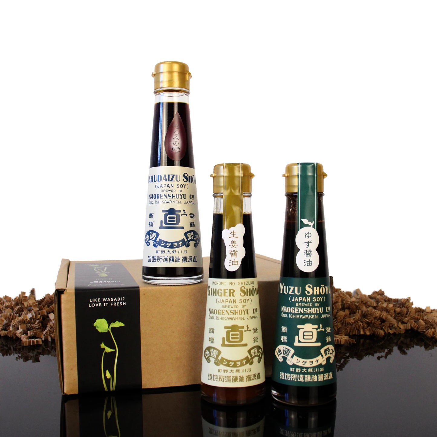 Three glass bottles from the Naogen Soy Sauce Gift Set, including yuzu and ginger varieties, displayed in front of a small cardboard gift box.