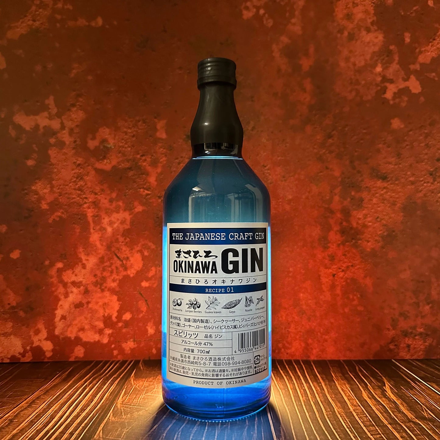 A 700ml bottle of Okinawa Gin, infused with unique Okinawan botanicals, stands on a wooden surface against an orange textured background.