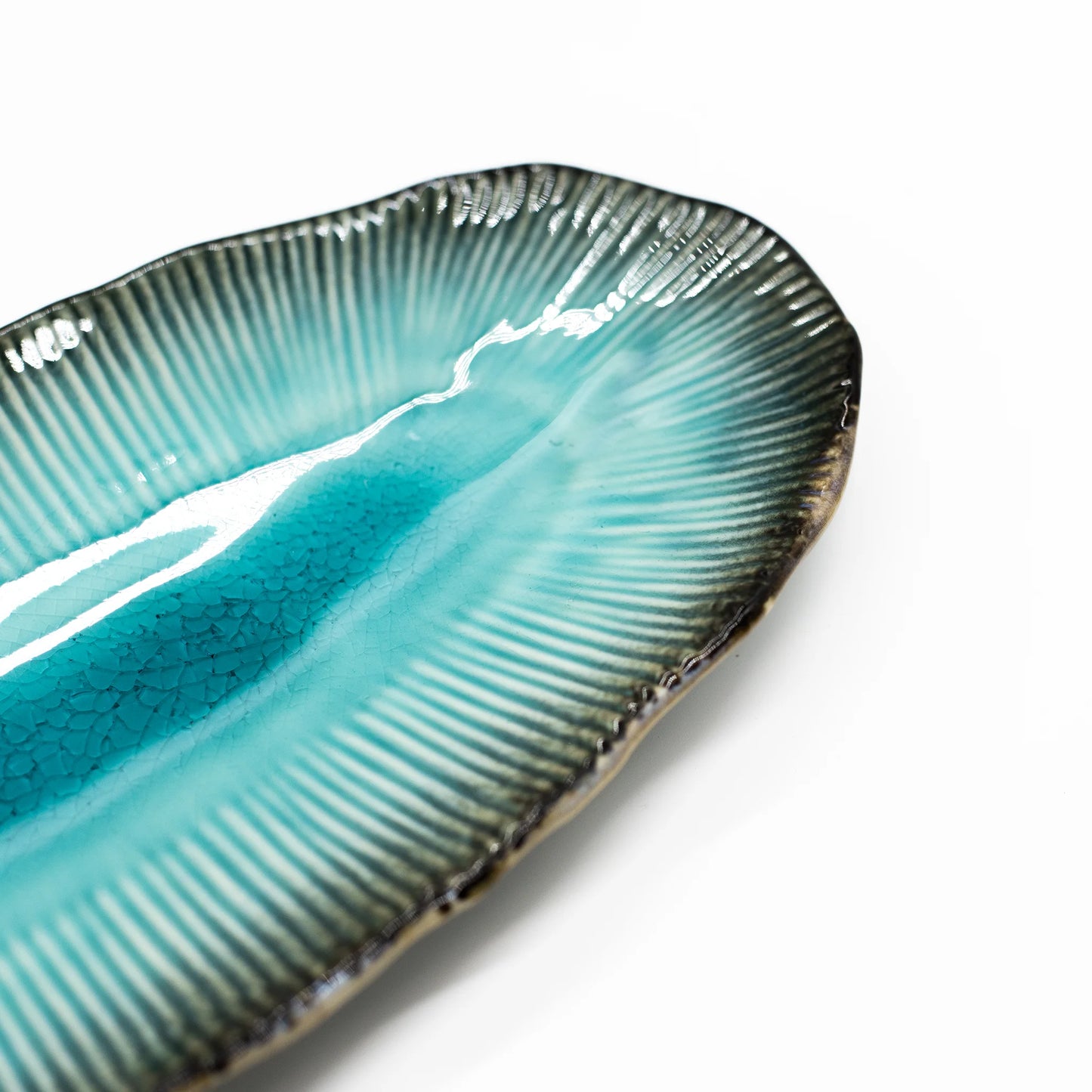 
                  
                    Close-up of the Sashimi Platter - Oval in Sky Blue 32cm, featuring textured, ribbed edges and a glossy blue-green gradient glaze, perfect for serving sashimi, set against a white background.
                  
                
