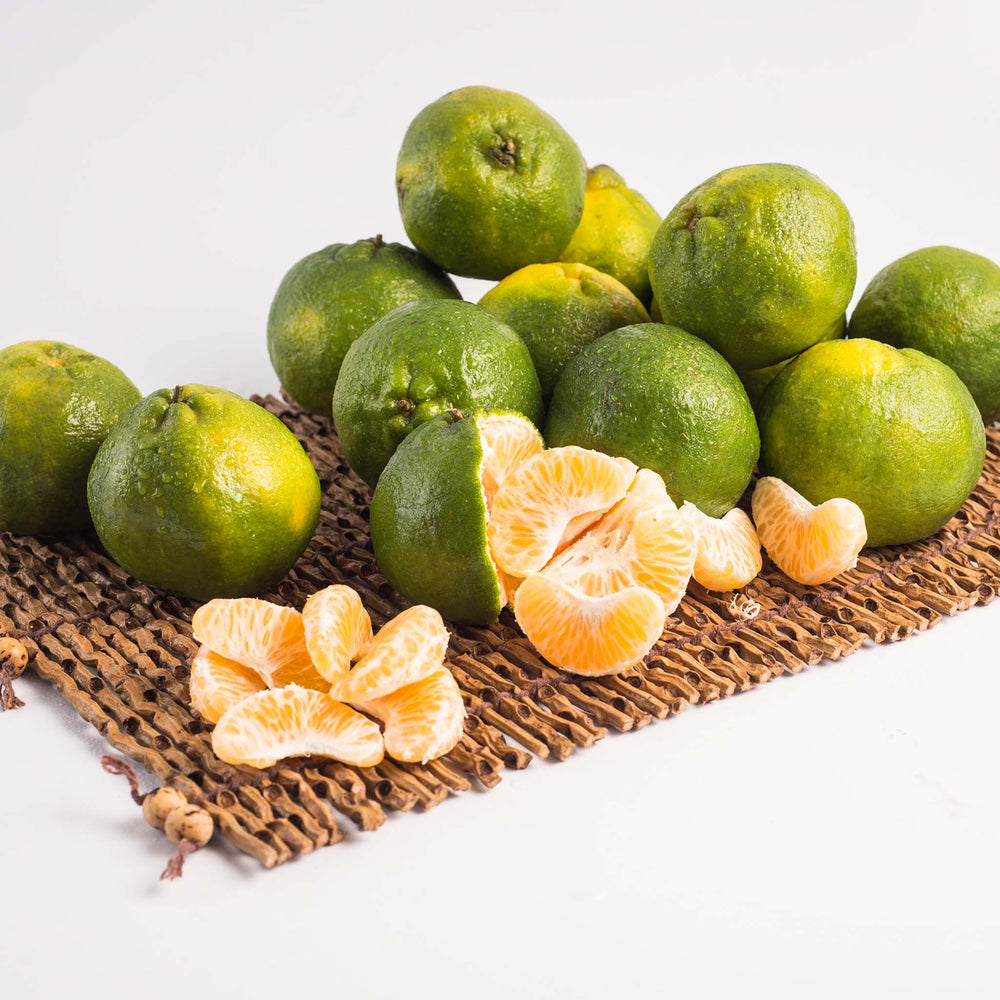 Fresh Ponkan Fruit, whole and peeled, are arranged on a woven mat against a white background, highlighting their vibrant color and expert cultivation.