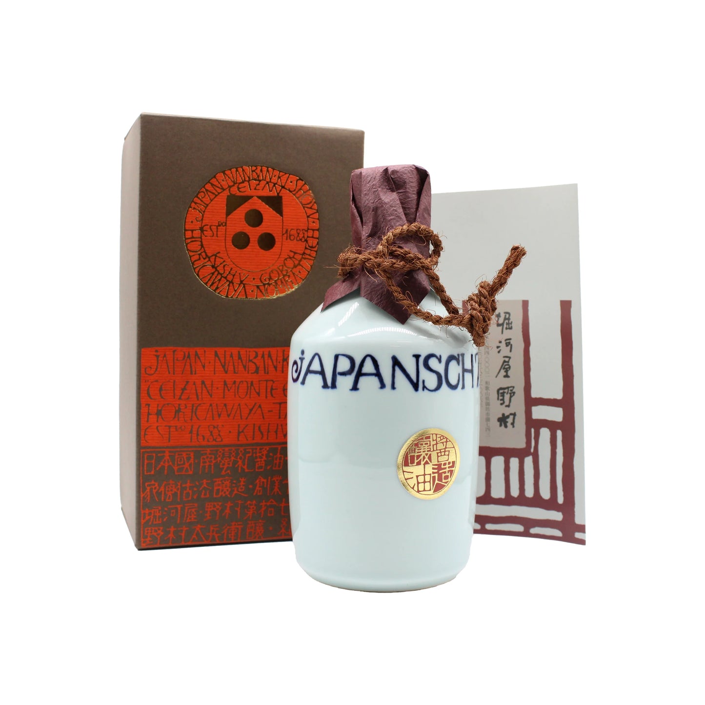 A white ceramic carafe labeled JAPANSCH, sealed with purple twine, sits beside a brown box and art card, showcasing the 900ml Premium Mitsuboshi Shoyu Soy Sauce made using the te-koji method.
