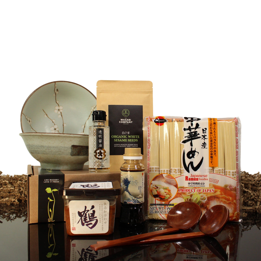 The Ramen Set with Ramen Bowls & Ladles includes Japanese ingredients like Hime Chuka Ramen Noodles, soy sauce, sesame seeds, cherry blossom bowls, wooden spoons, and more, all displayed on a reflective surface.