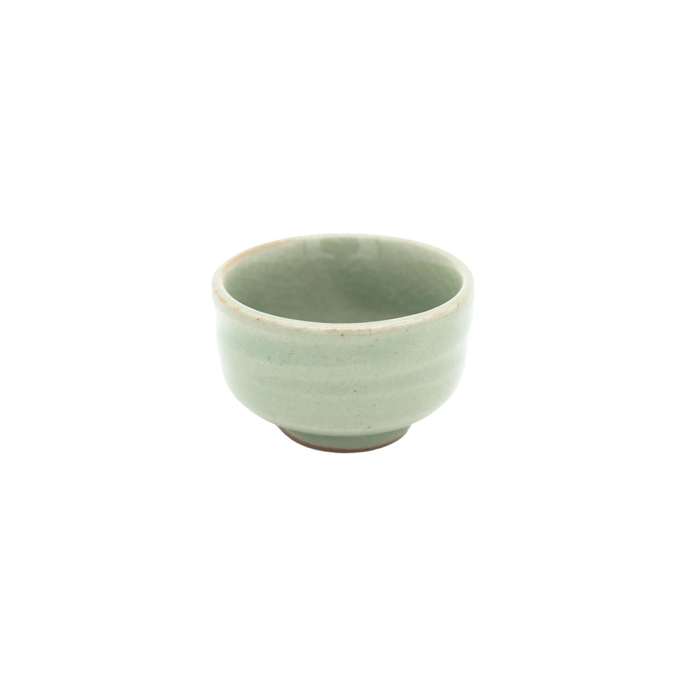 The Sake Cup - Celadon Green is a small, round cup made from Minoyaki porcelain, featuring a light green celadon glaze and a slightly flared rim, displayed on a plain white background.