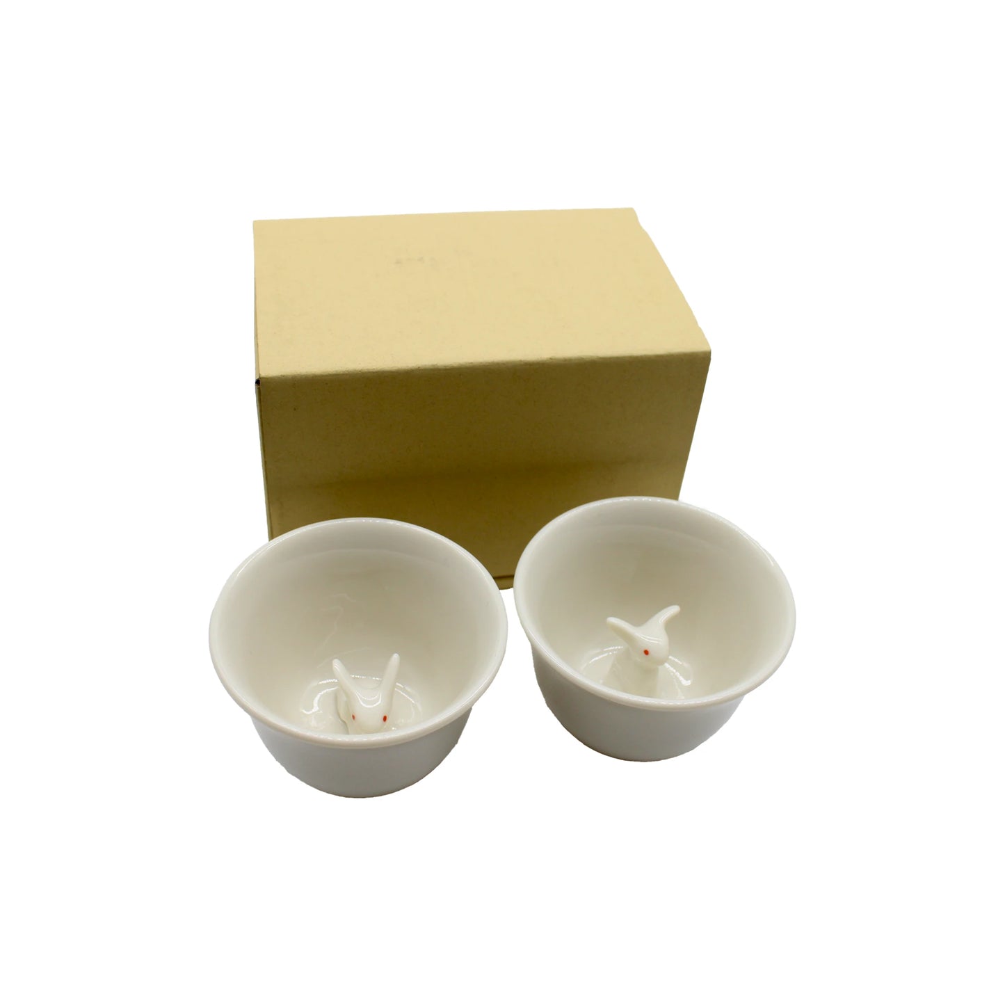 
                  
                    The Sake Cup Boxed Set - Rabbit Design features two white ceramic Japanese sake cups, each adorned with a delightful rabbit motif inside, presented alongside a simple beige cardboard box on a white background—an elegant gift set suitable for any occasion.
                  
                