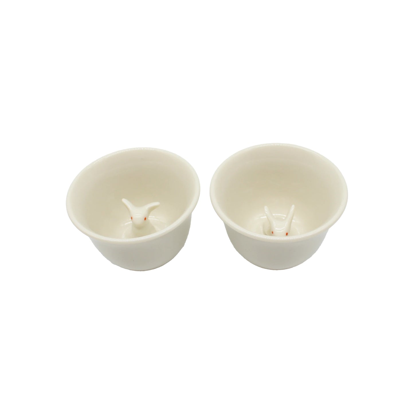 
                  
                    The Sake Cup Boxed Set - Rabbit Design features two white ceramic cups, each adorned with a small rabbit motif and a delightful rabbit head figurine nestled at the bottom. Presented side by side on a white background, these charming cups make an ideal gift set or serve as unique Japanese sake cups for special occasions.
                  
                