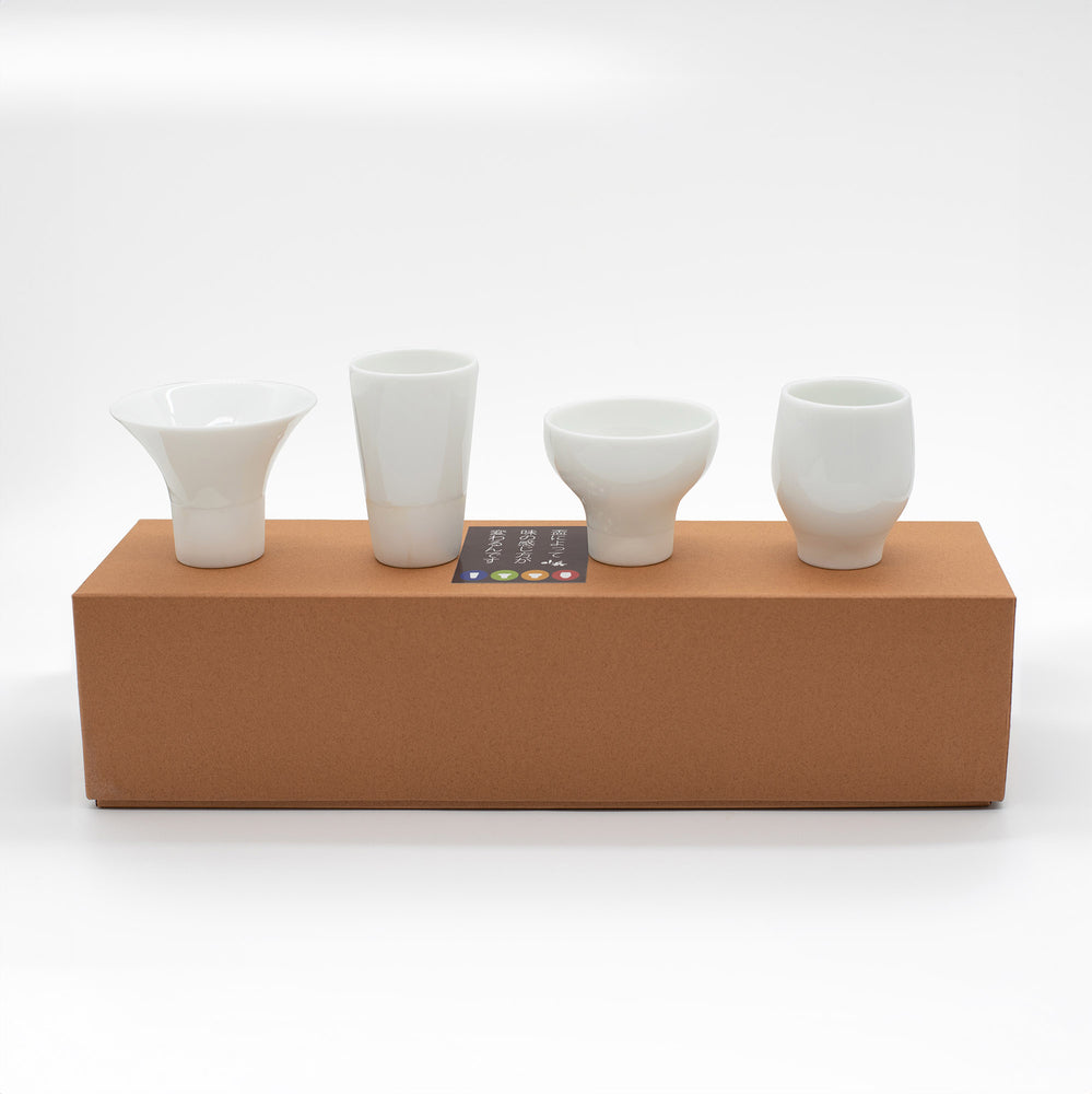 The Sake Cups Tasting Boxed Set features four unique white ceramic cups, beautifully crafted and displayed in a row on a brown box—ideal for an elegant sake tasting experience.