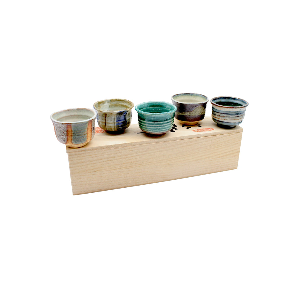 
                  
                    The Ochoko Sake Cups - Set of 5 features small cups with unique earthy and blue-green glazes, displayed on a rectangular light wooden box, reflecting Japanese ceramic tradition against a white background.
                  
                