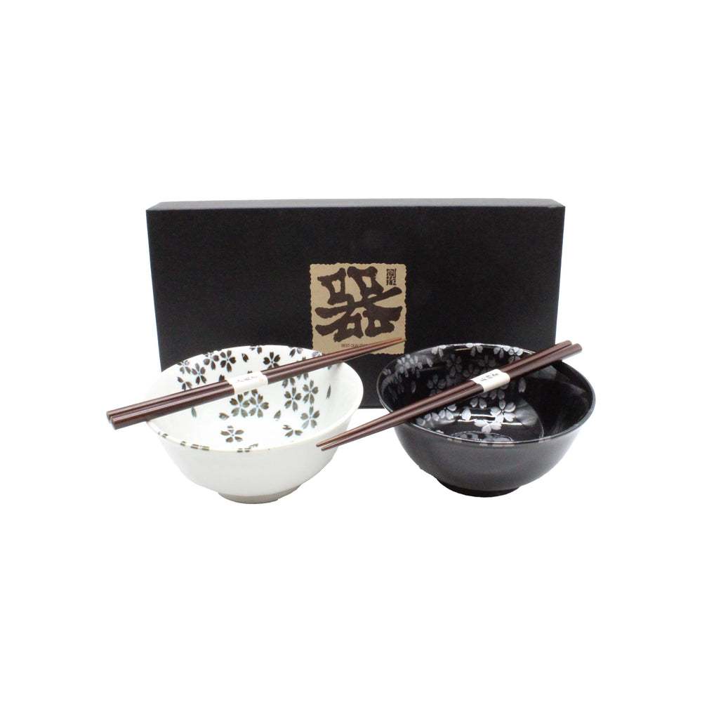 The Sakura Blossom Bowls Gift Set – Black & White includes two ceramic bowls with sakura motifs (one white, one black), each paired with chopsticks and presented in a black box with Japanese writing.