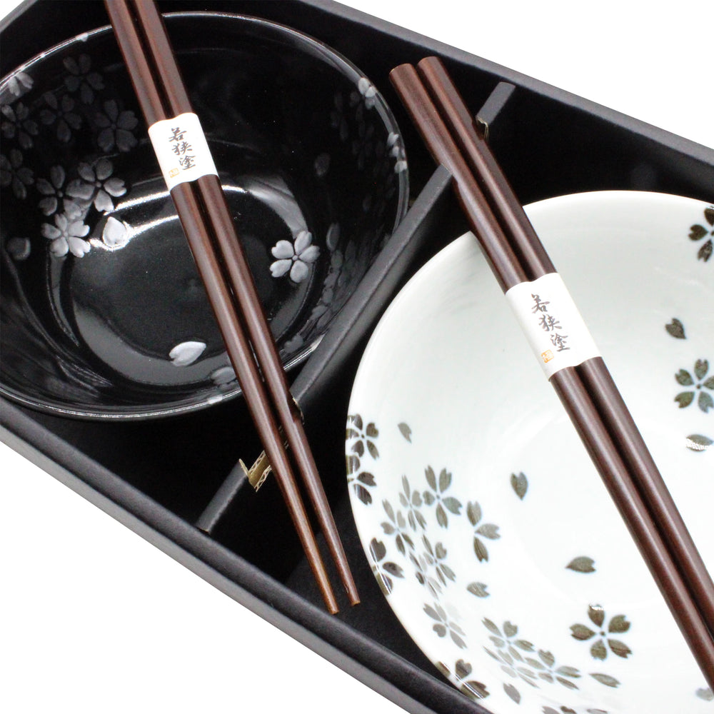 The Sakura Blossom Bowls Gift Set – Black & White features a black tray with two pairs of chopsticks, a black ceramic bowl with a sakura motif, and a matching white bowl.