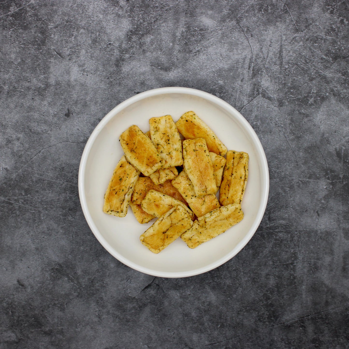
                  
                    A white bowl filled with Japanese Rice Crackers - Senbei Seaweed & Soy Sauce 80g, featuring rectangular, seasoned pieces, sits on a gray, textured surface.
                  
                