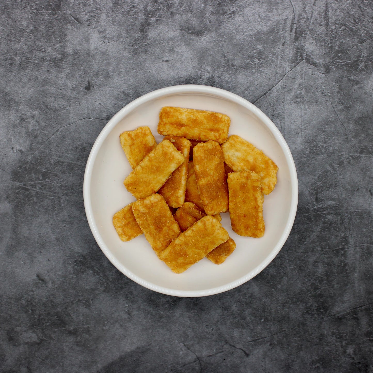 
                  
                    A white plate with several rectangular, golden brown Japanese Rice Crackers - Senbei Kinako Soybean Flour 80g rests on a dark gray textured surface.
                  
                