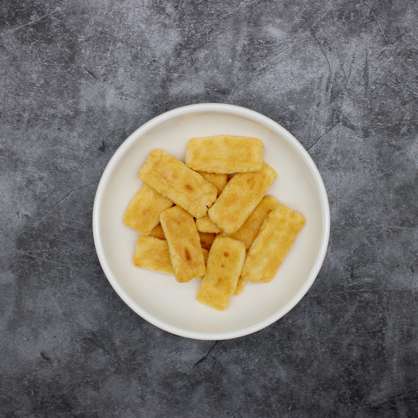 
                  
                    A white bowl filled with Japanese Rice Crackers - Senbei Sweet & Spicy 80g, featuring rectangular, golden-brown pieces, sits on a dark, textured surface.
                  
                