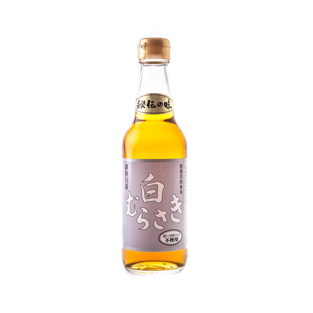 A clear glass bottle of Shiro Murasaki White Soy Sauce, filled with amber white soy sauce, sealed with a gold cap, and labeled in Japanese on a lavender background.