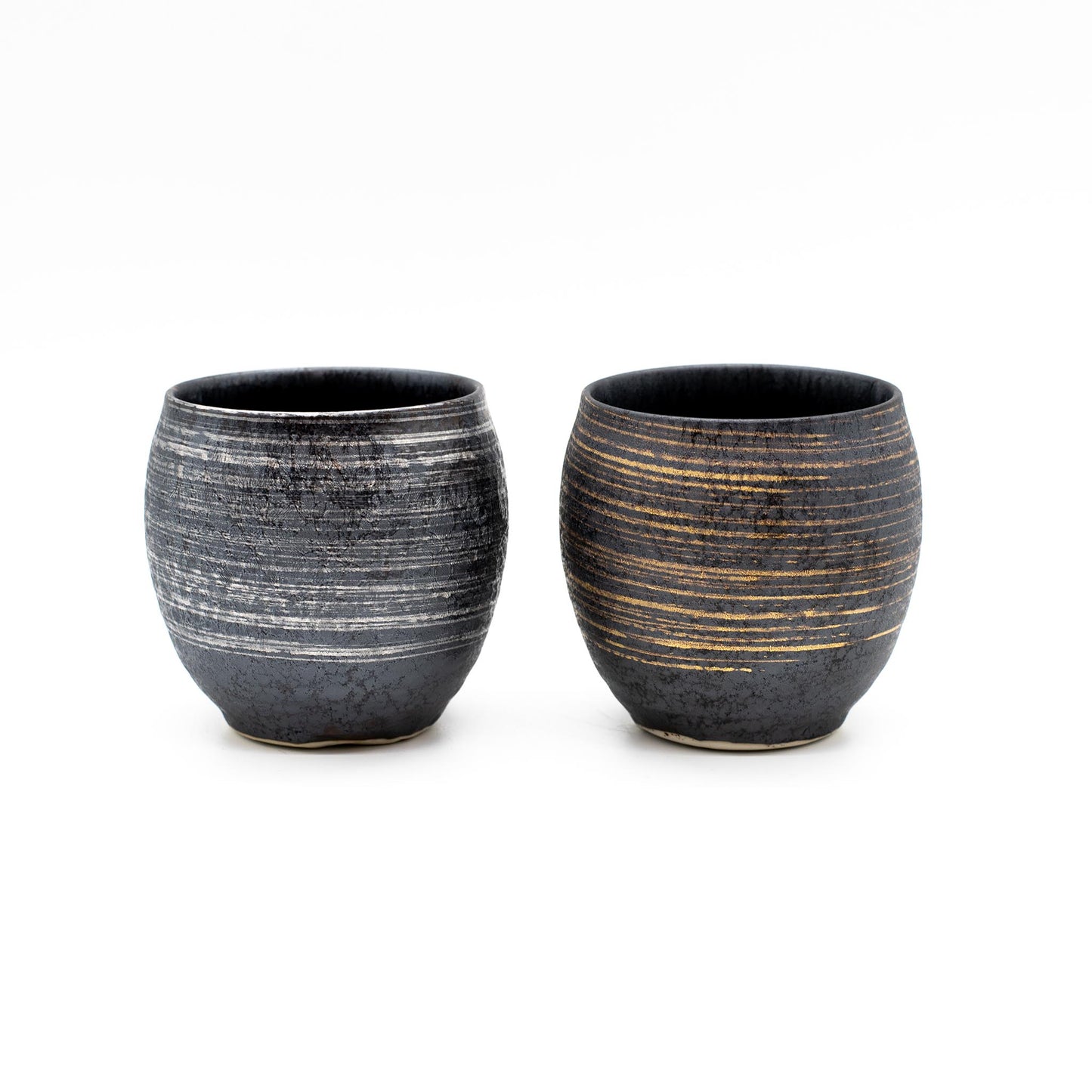 The Sho-Chu Cups - Boxed Set Of 2 includes round Minoyaki porcelain cups with textured lines—one featuring a silver pattern, the other gold—displaying refined Japanese craftsmanship, side by side on a white background.