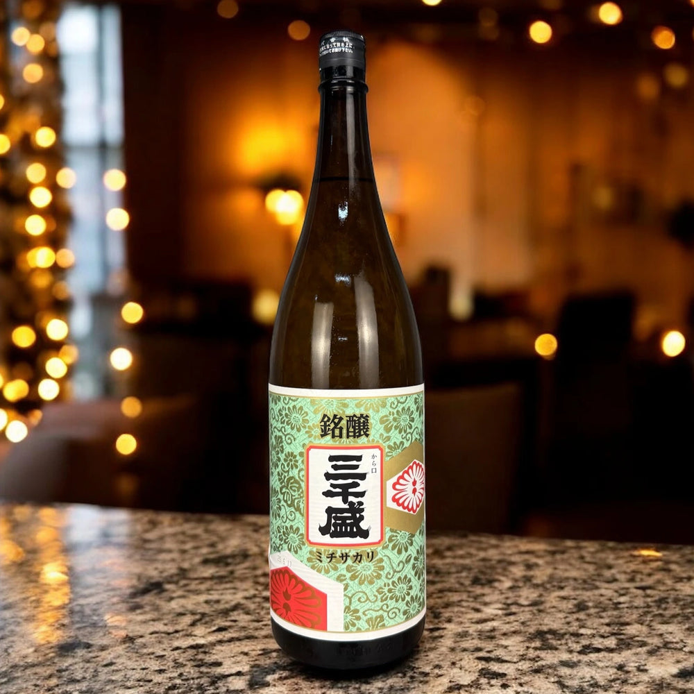 A 1.8L Signature Brew Sake bottle with a patterned green and white label featuring Japanese characters is displayed on a granite countertop in a dimly lit room.