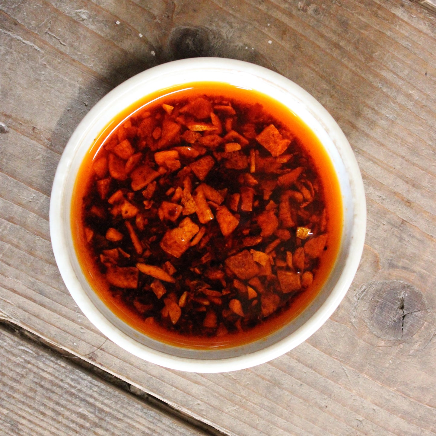 
                  
                    A white bowl containing Momoya Taberu Mild La-Yu Chilli Oil (110g) with chopped garlic pieces sits on a wooden surface.
                  
                