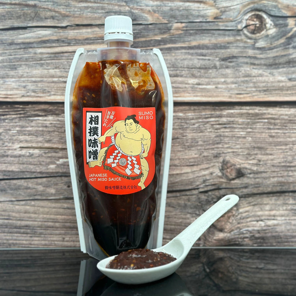 A 360g pouch of Sumo Spicy Miso Sauce stands upright, with a white spoon in front showcasing the thick, dark sauce and its bold umami flavor.