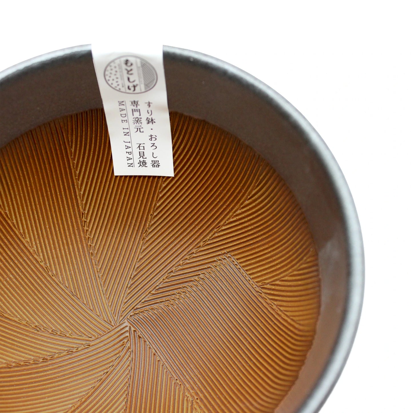 
                  
                    The Suribachi Motoshige Pestle & Mortar - Black is a ceramic bowl featuring a textured, geometric interior inspired by traditional Japanese design, and comes with a white "MADE IN JAPAN" label.
                  
                