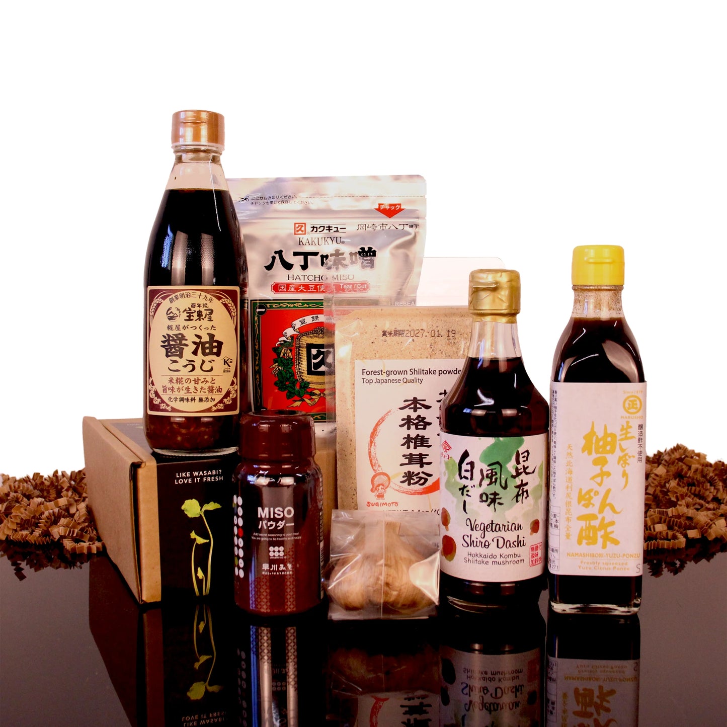 The Japanese Umami Box featuring bottles of soy sauce and ponzu, a bag of miso, shiitake powder, and dried mushrooms arranged in front of its packaging.