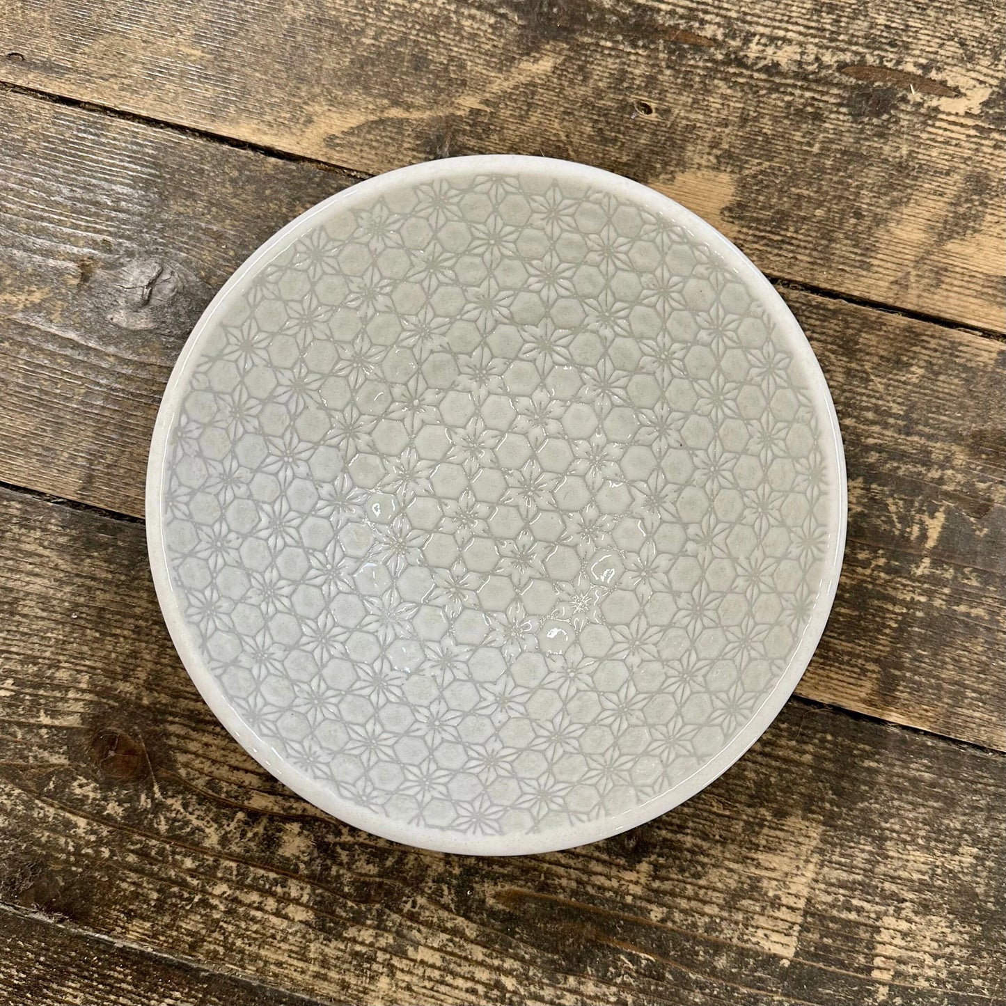 
                  
                    The Udon Bowl - White Star, a handmade ceramic bowl with a subtle floral geometric pattern, sits on a rustic wooden surface. Microwave safe for daily use.
                  
                