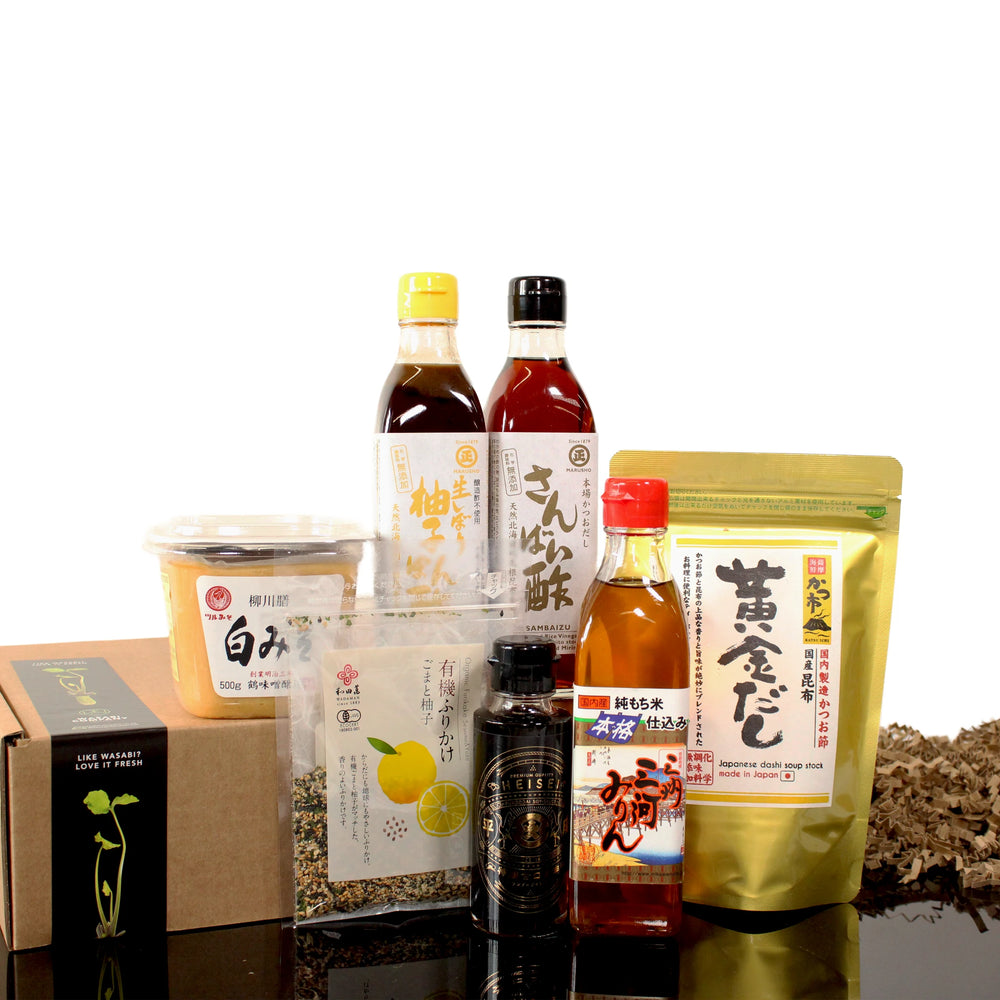 The Ultimate Japanese Cooking Collection features essential pantry staples like soy sauce, white miso paste, sauces, seasonings, bottled liquids, and a box—perfect for creating authentic Japanese dishes—all arranged on a white background.