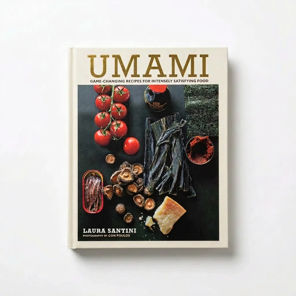 The Umami by Laura Santini cookbook features an overhead shot of umami-rich ingredients like tomatoes, mushrooms, seaweed, and anchovies on a dark background.