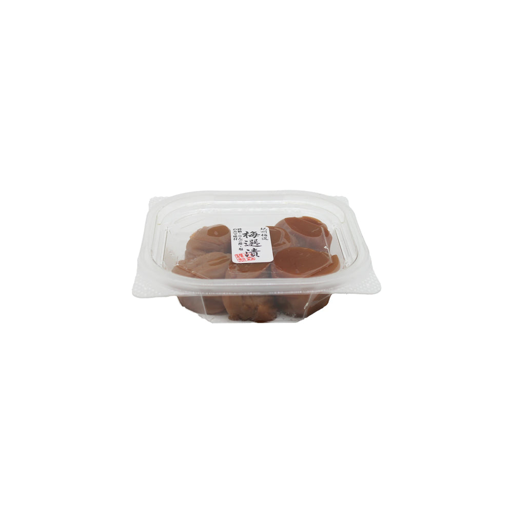 A clear plastic container of Umeboshi Plum, filled with brown plums and topped with a white lid label featuring Japanese text, is photographed against a white background.